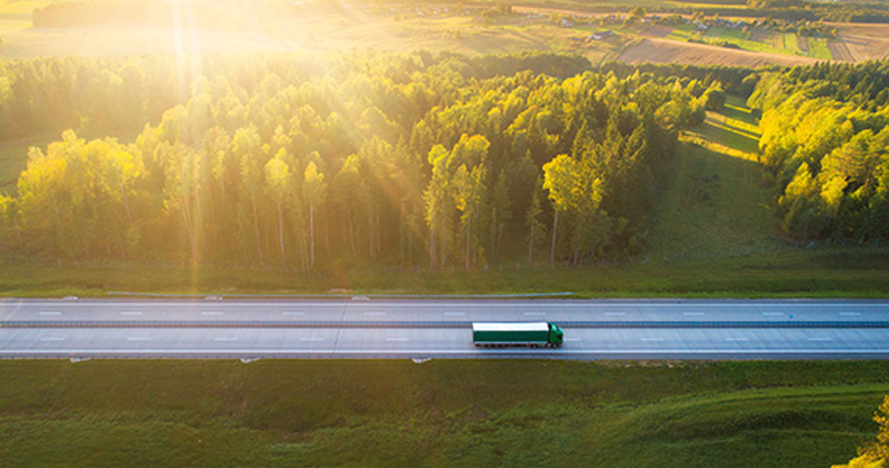 Truck driving on a road through green scenery in the sunset